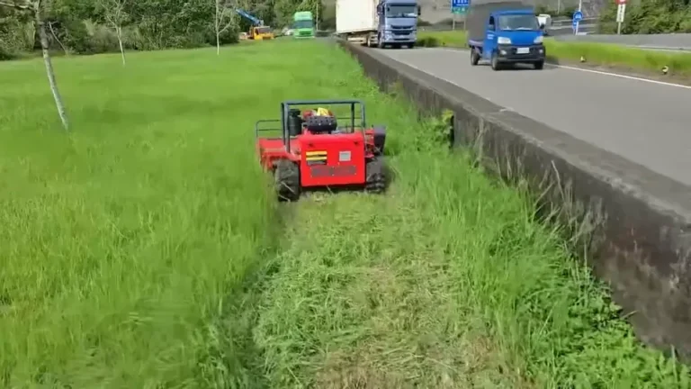 Remote mower maintaining a narrow grass drainage strip beside a road wall
